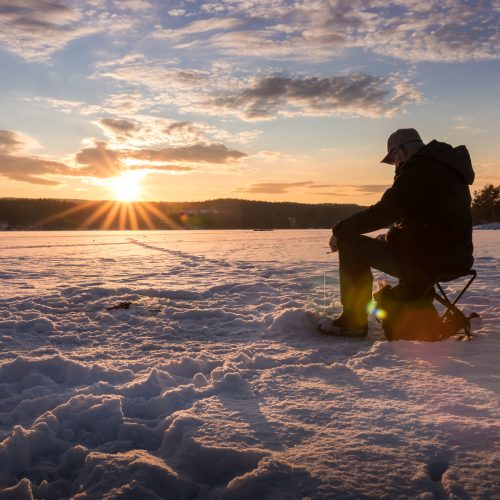 Ice fishing on a lake in Norway at sunset.